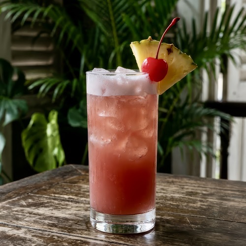 Singapore Sling cocktail garnished with pineapple slice and cherry.
